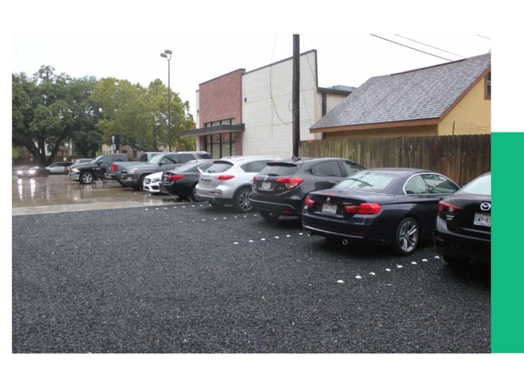 Parking lot with vehicles on a wet paved surface in front of buildings.